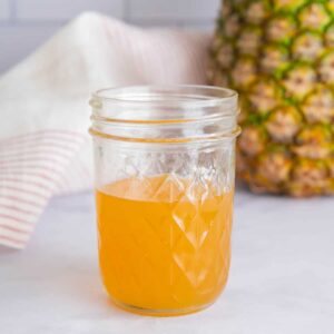 Pineapple ginger syrup (Starbucks copycat) in a glass jar with a pineapple.