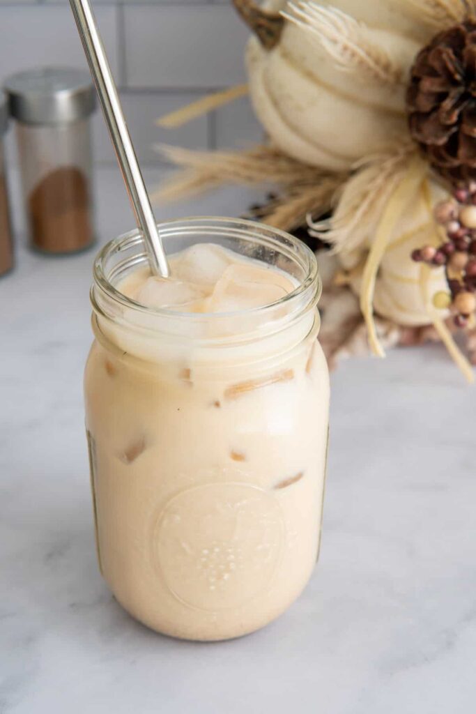 Pumpkin spice iced latte in a glass mason jar with a metal straw and fall decorations.