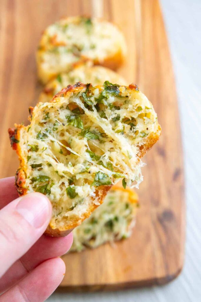 A slice of stuffed garlic bread being held up in front of a wooden board.