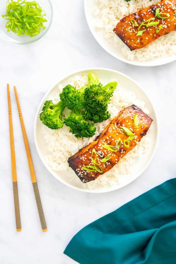 Air fryer teriyaki salmon on a white plate with chopsticks and a teal napkin.
