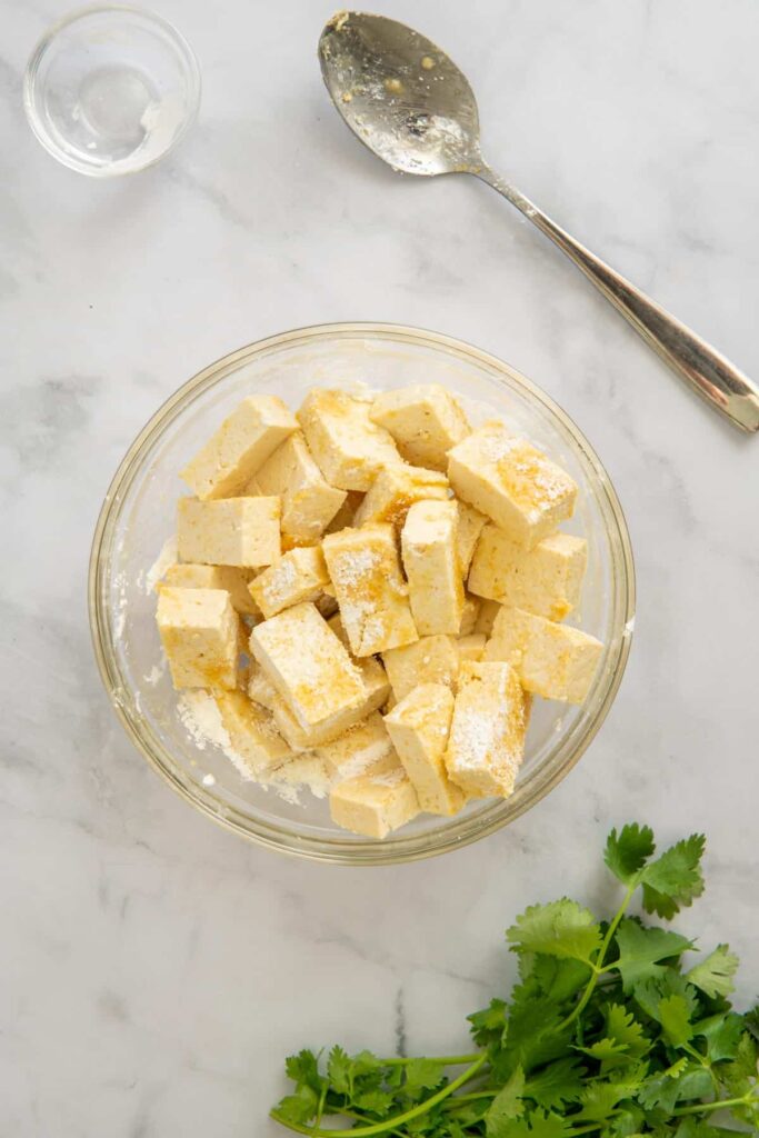 Tofu in a glass bowl coated with seasonings and corn starch.