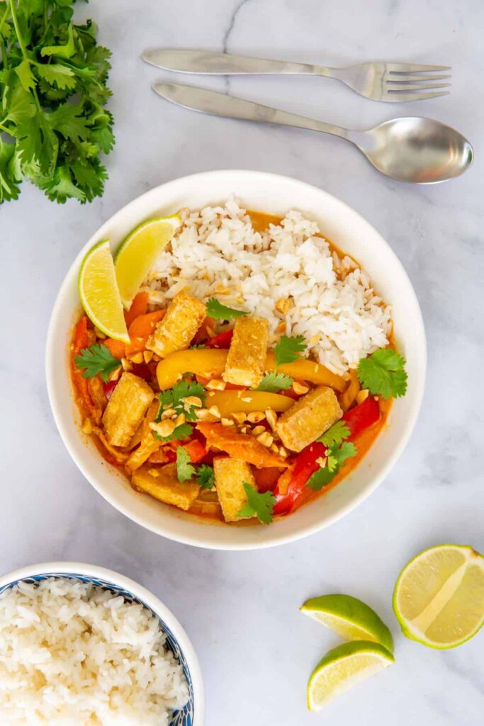 Vegan Thai red curry with tofu in a white bowl with rice, lime, and cilantro.