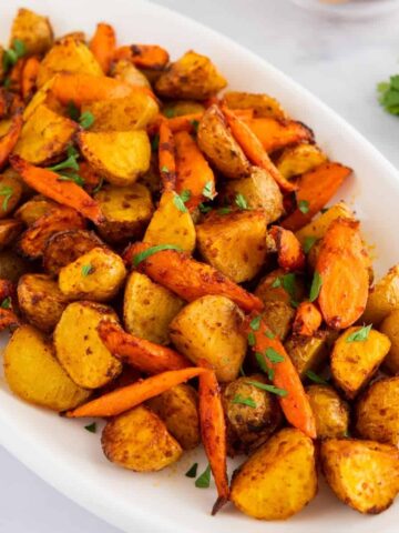 Air fryer potatoes and carrots on a white platter with parsley.