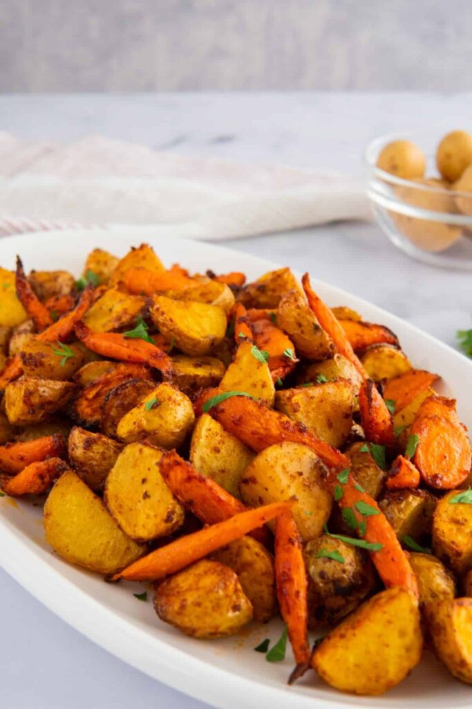 Air fryer potatoes and carrots on a white platter in front of a grey background.