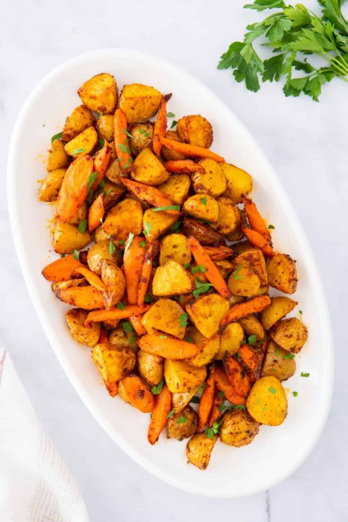 An overhead shot of air fryer potatoes and carrots on a white platter.