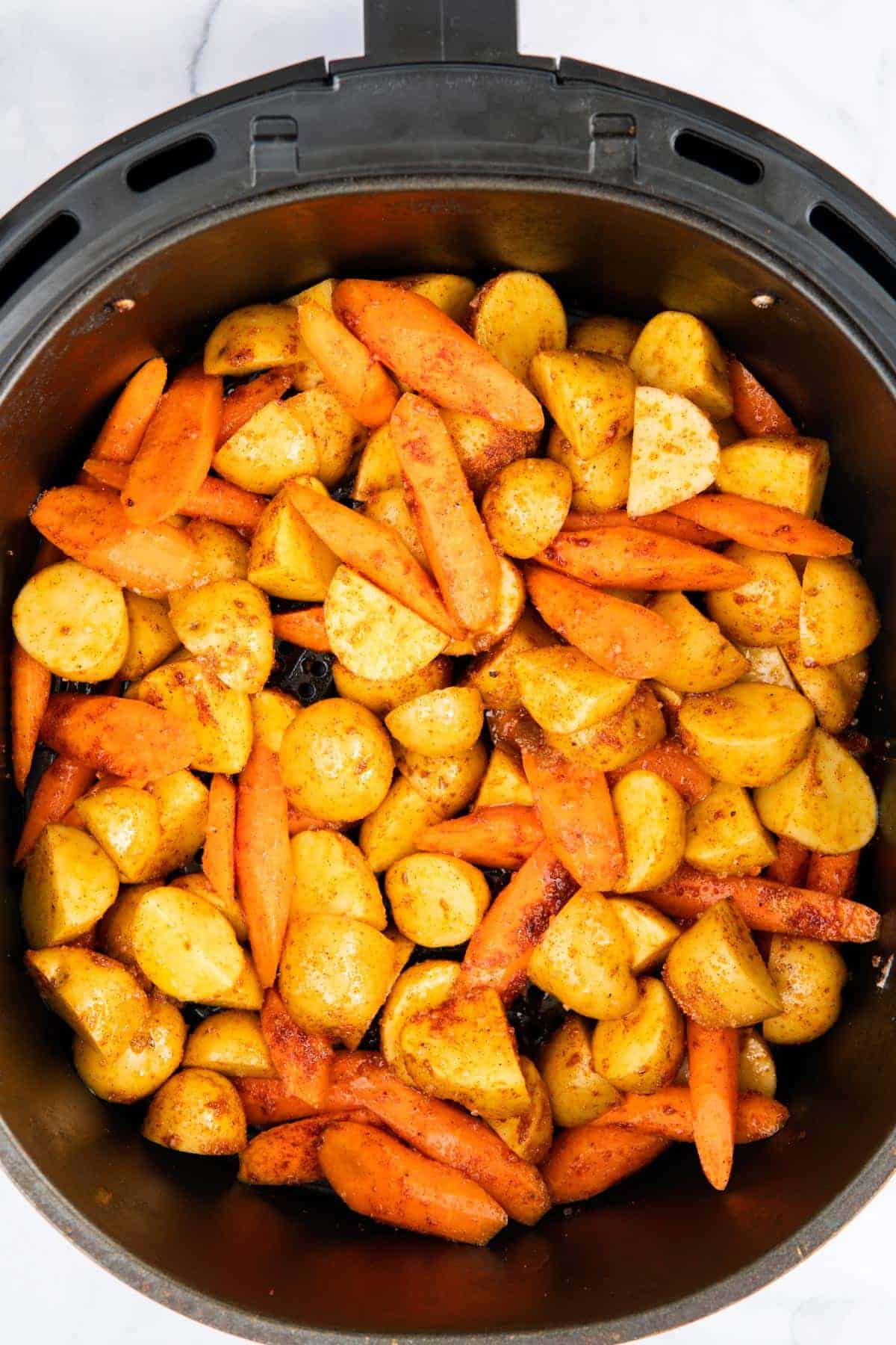 Potatoes and carrots in an air fryer basket.