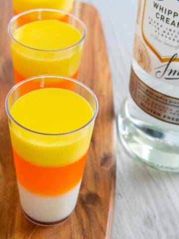 Halloween candy corn jello shots on a wooden board next to vodka.