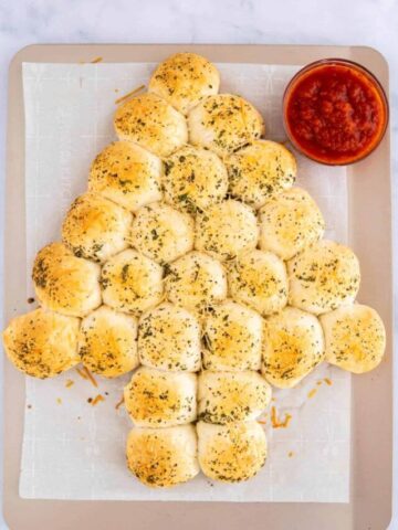 Easy cheesy Christmas tree pull apart bread on a baking sheet next to a glass bowl of marinara sauce.