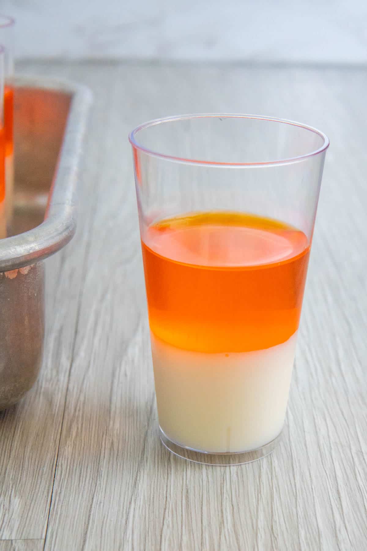 White and orange layers of candy corn jello shot in a plastic shot glass.