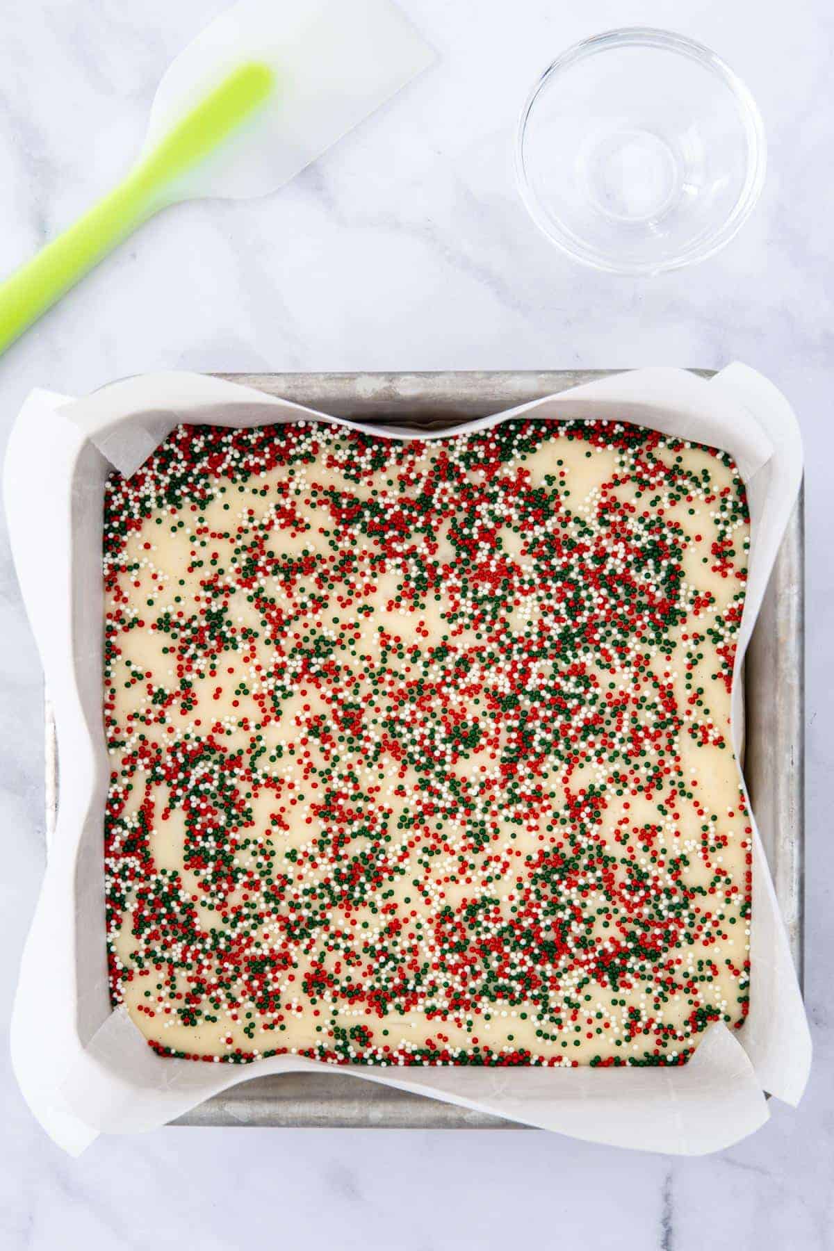 Sugar cookie fudge in an 8x8 inch pan with Christmas sprinkles on top.