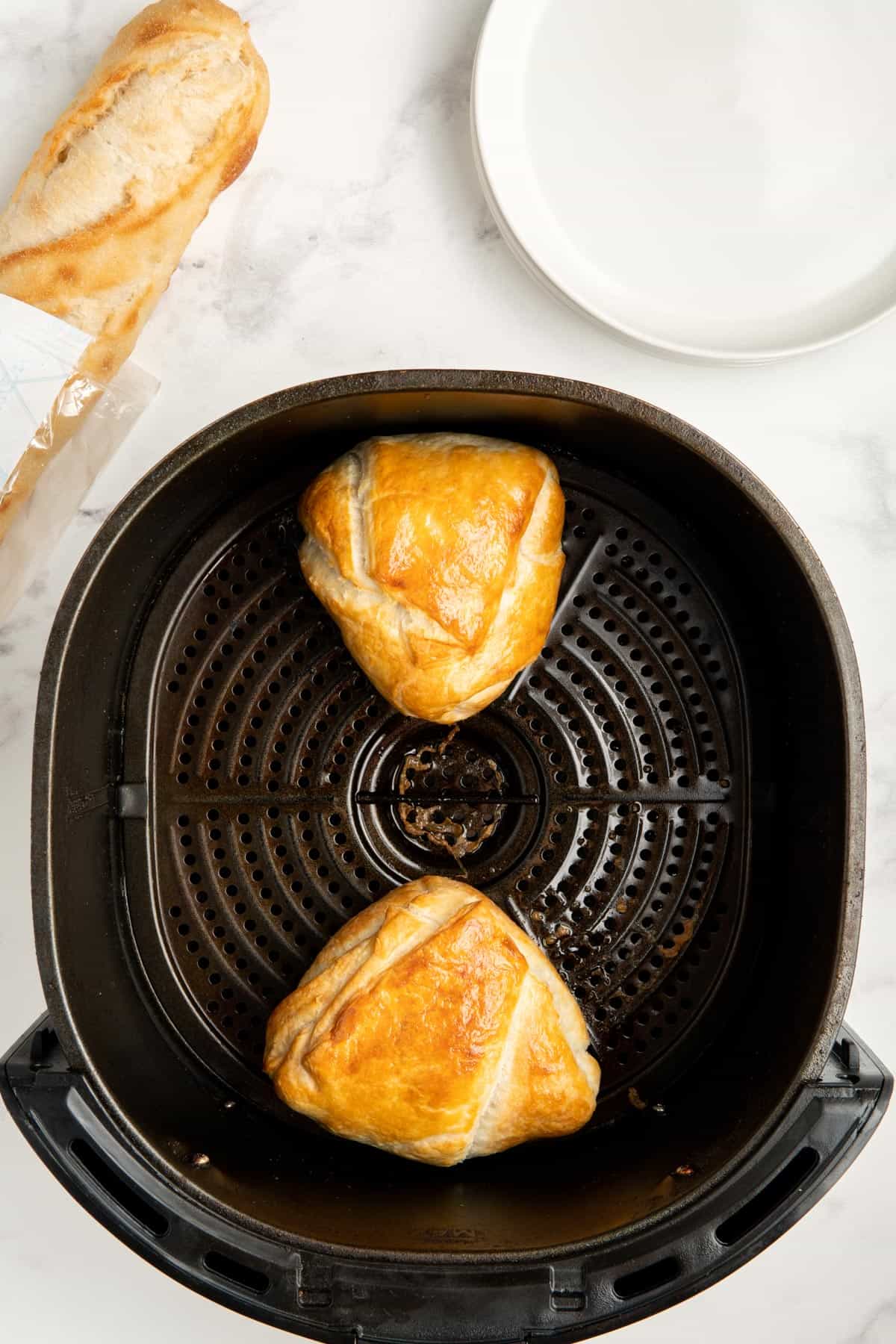 Two wedges of cooked puff pastry wrapped brie in an air fryer basket.