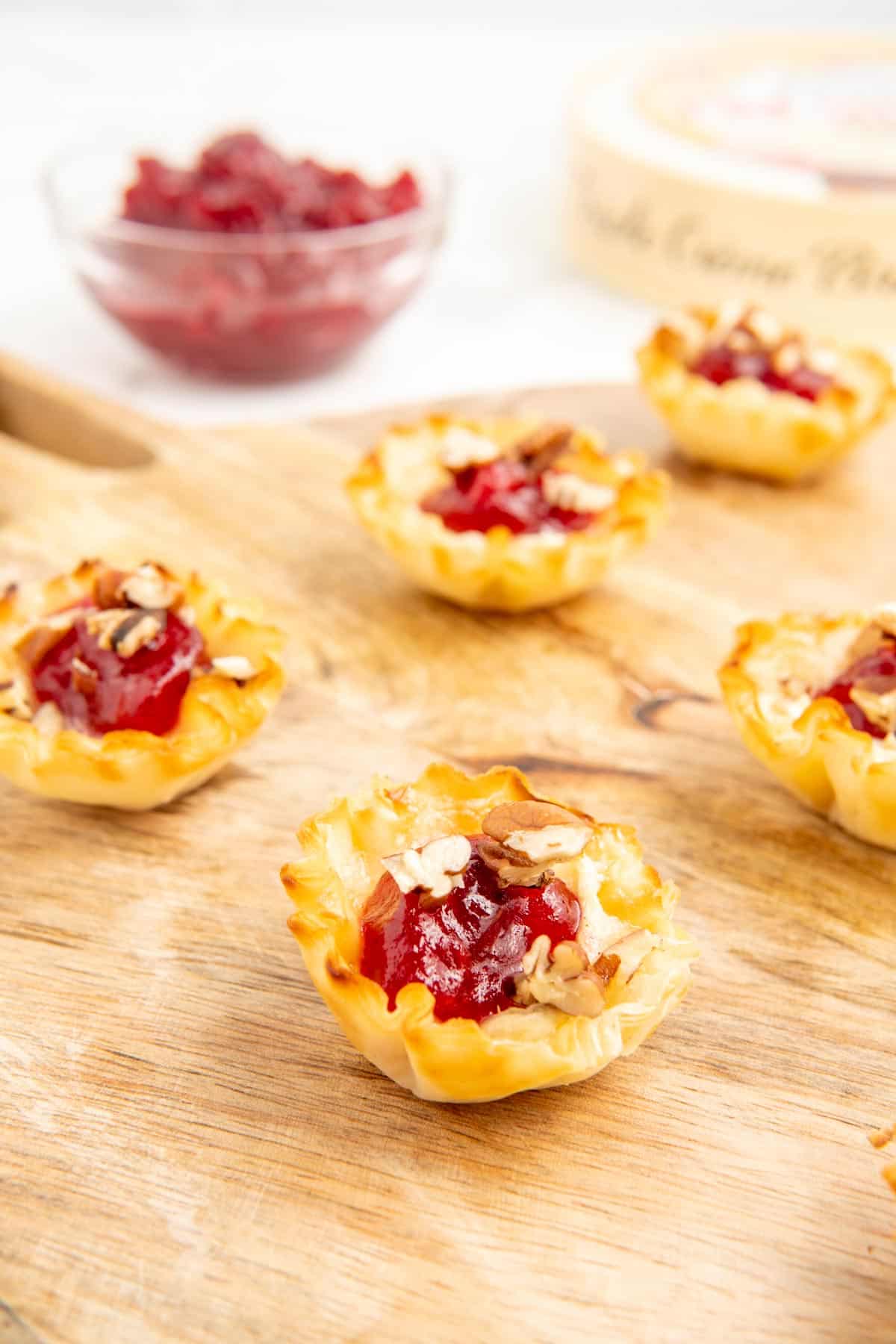 A close-up shot of air fryer brie bites with cranberry sauce and chopped pecans on a wooden board.