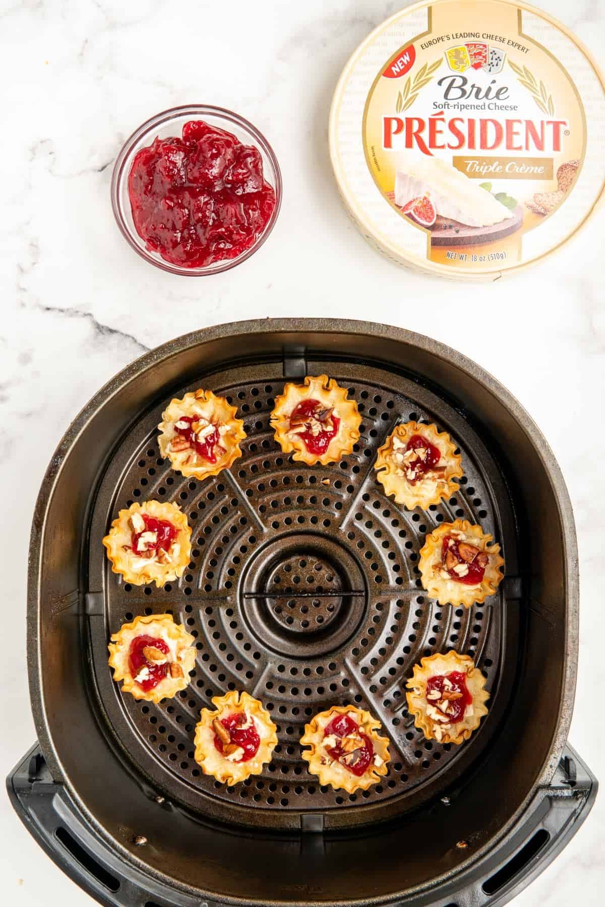 Air fryer brie bites topped with cranberry sauce and pecans in an air fryer basket.