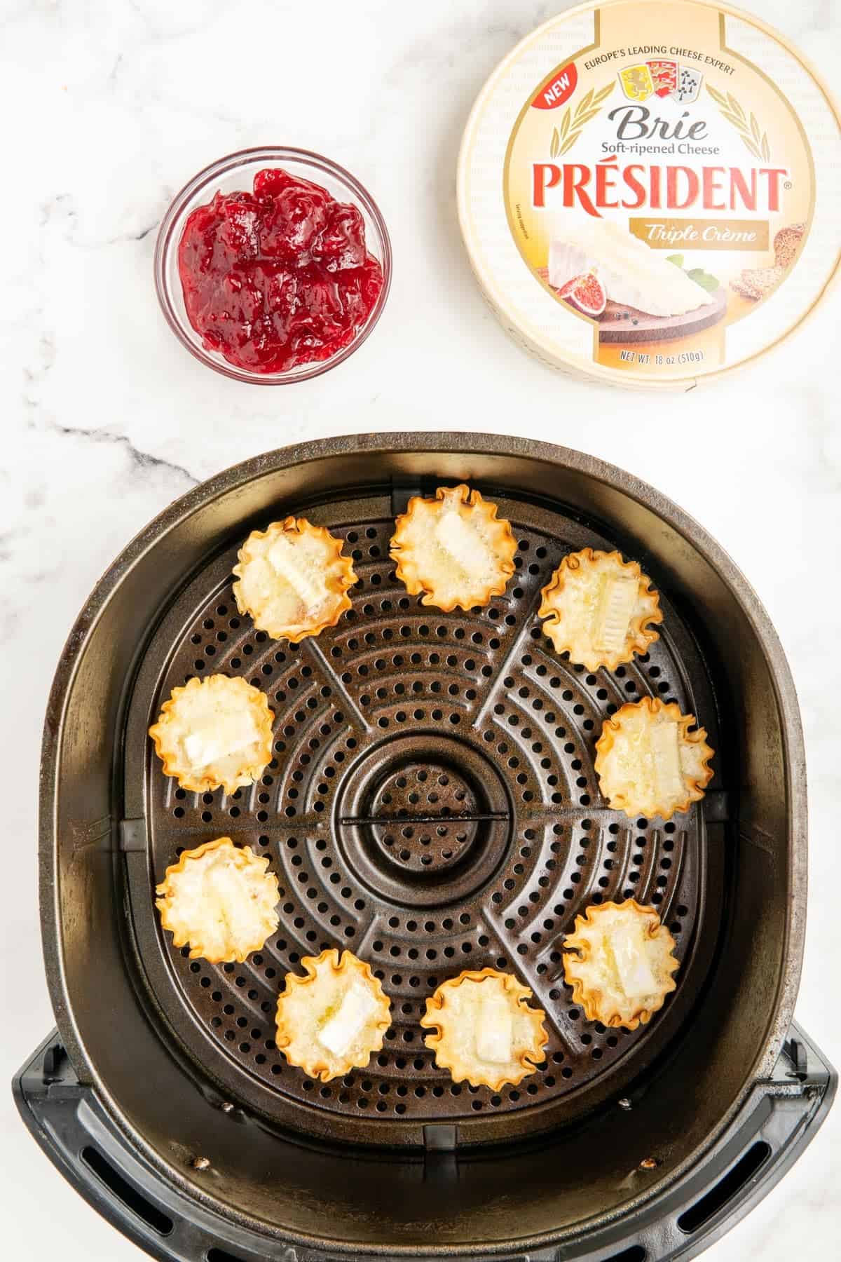 Phyllo shells filled with melted brie cheese in an air fryer basket.