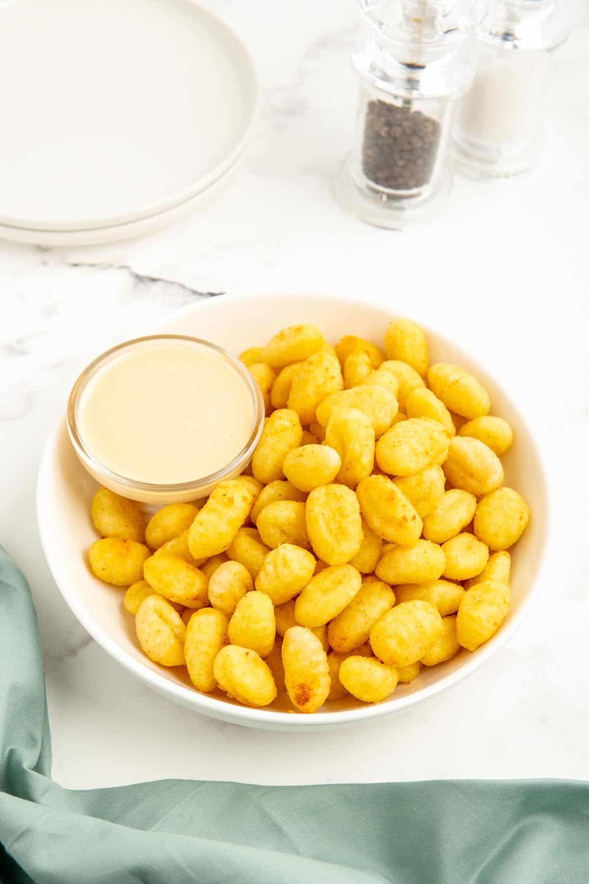 Air fryer gnocchi in a white bowl with sauce and a mint napkin.