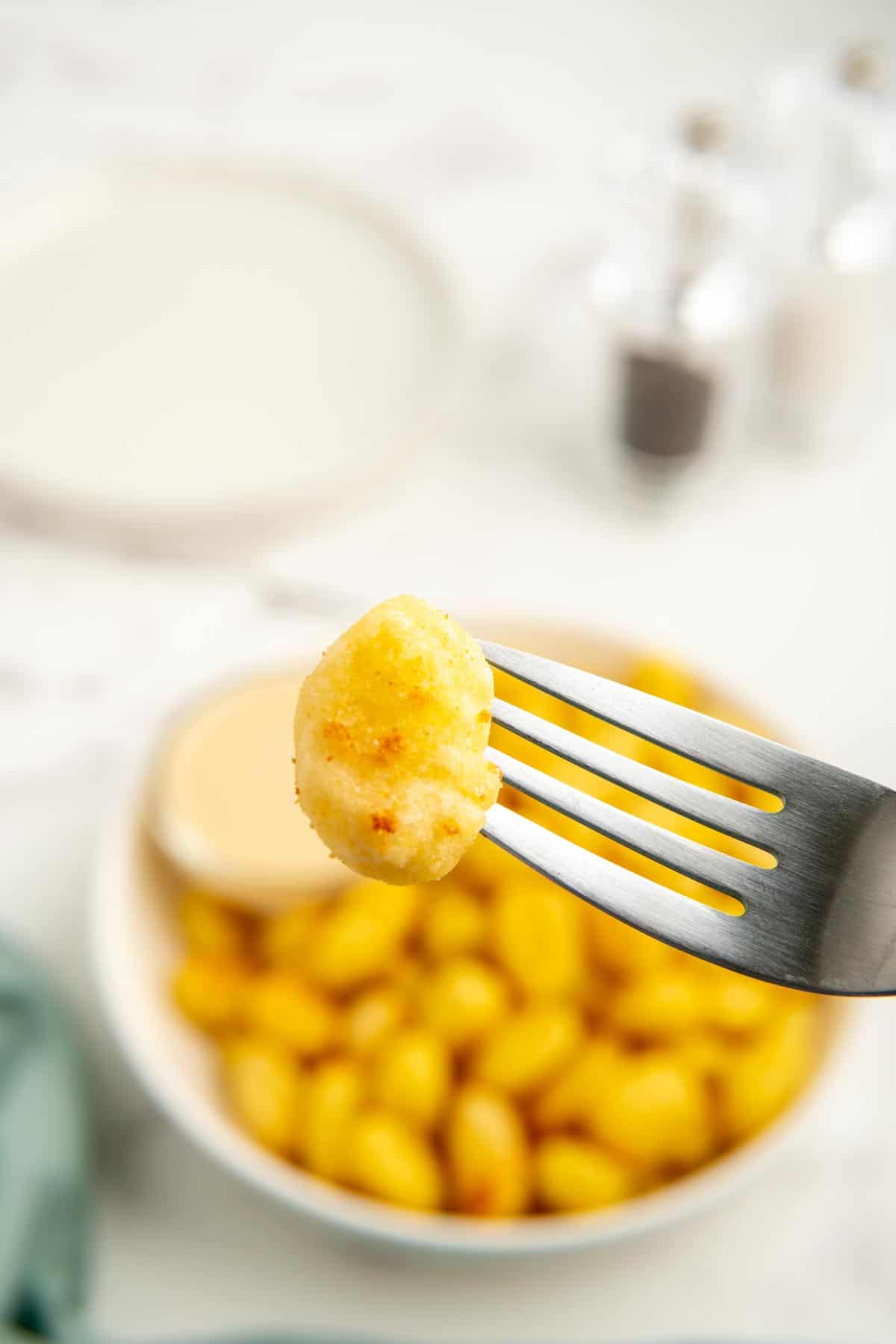 A piece of air fryer gnocchi on a fork in front of a bowl of air fryer gnocchi.