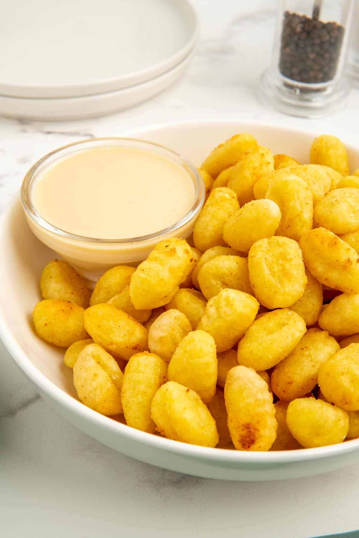 A close-up shot of air fryer gnocchi in a white bowl with maple mustard sauce.