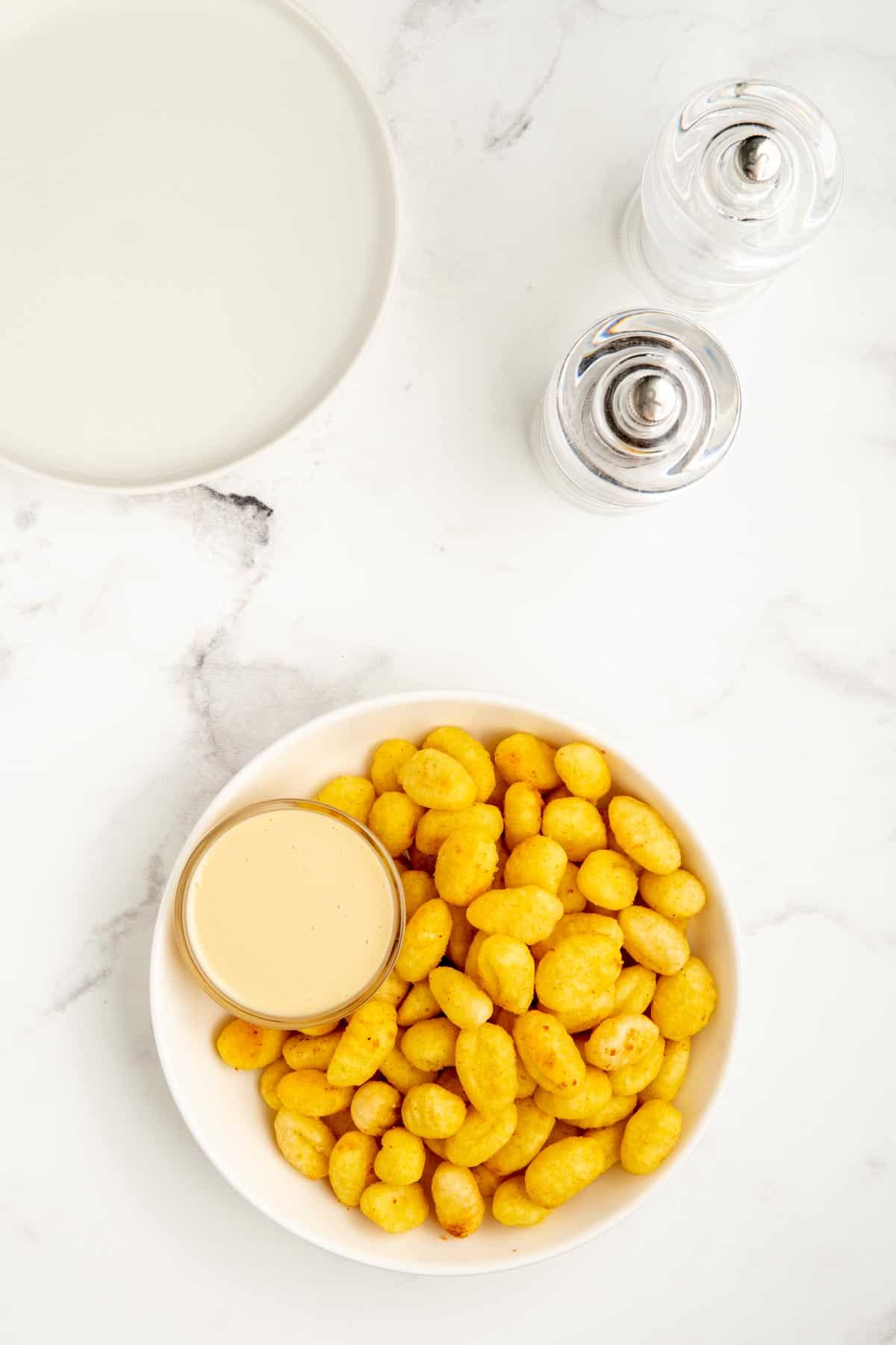 An overhead shot of air fryer gnocchi in a white bowl with salt and pepper mills.
