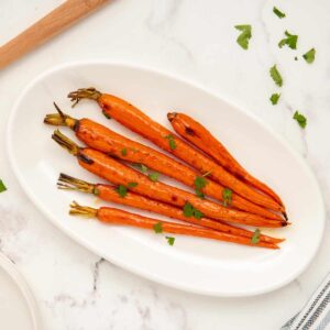 Brown sugar honey glazed carrots served on a white oval-shaped platter.