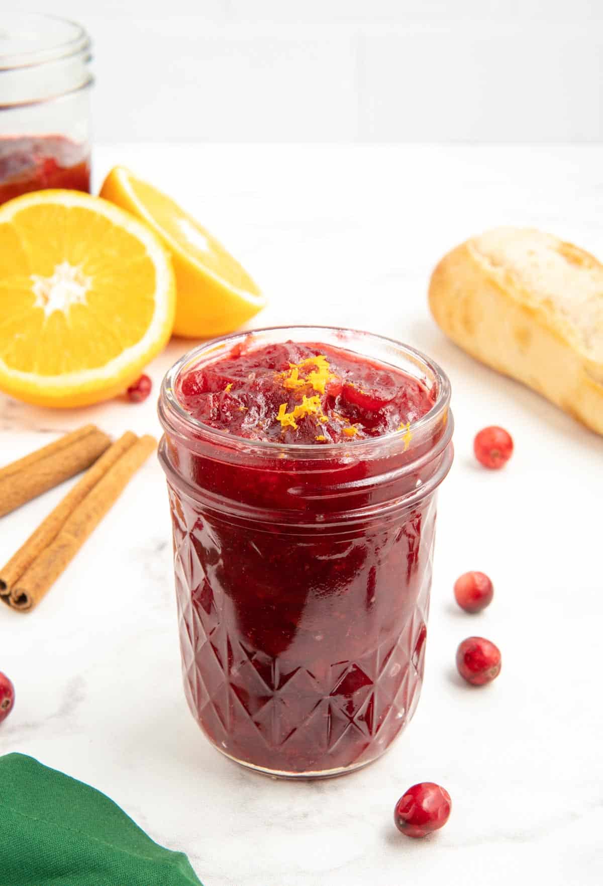 Cranberry sauce made with orange juice in a glass jar with cranberries scattered around.