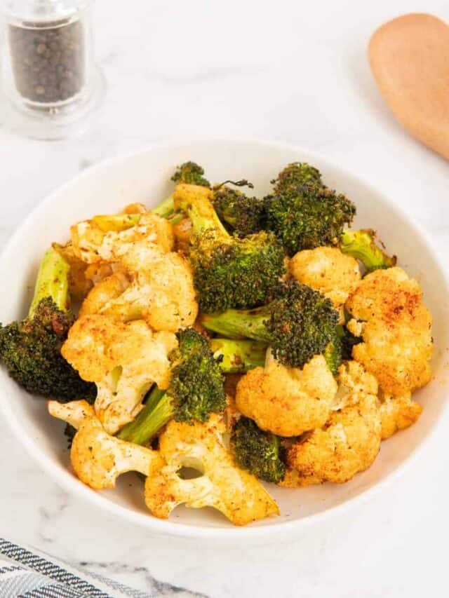 Air fryer broccoli and cauliflower in a white bowl with a wooden spoon in the background.