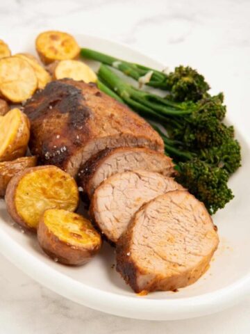 Pork tenderloin slices on a serving platter surrounded by potatoes and tender stem broccoli.