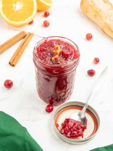 A spoonful of cranberry sauce with orange juice next to a jar of cranberry sauce.