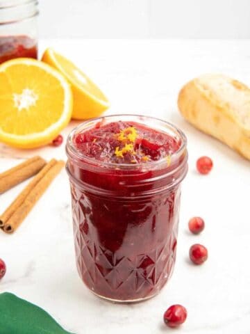 Cranberry sauce made with orange juice in a glass jar with cranberries scattered around.