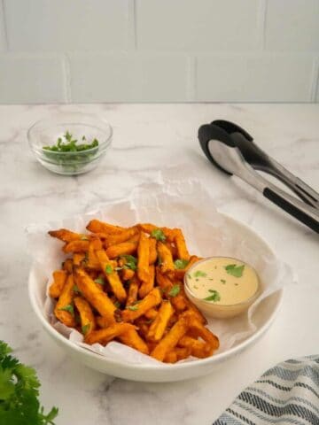 Air fryer sweet potato fries in a white bowl with subway tile background.