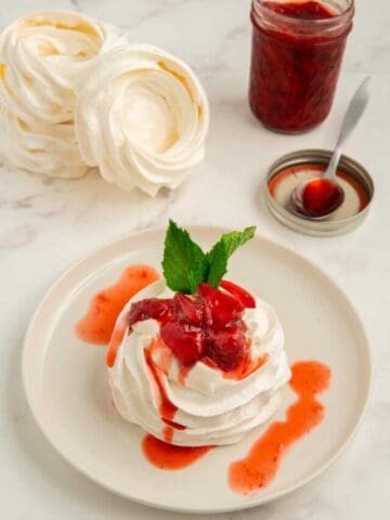 A mini pavlova nest topped with strawberry compote and mint with unfilled pavlova nests in the background.