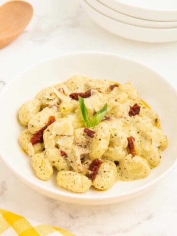 A bowl of pesto gnocchi served with extra sun-dried tomatoes and garnished with fresh basil.