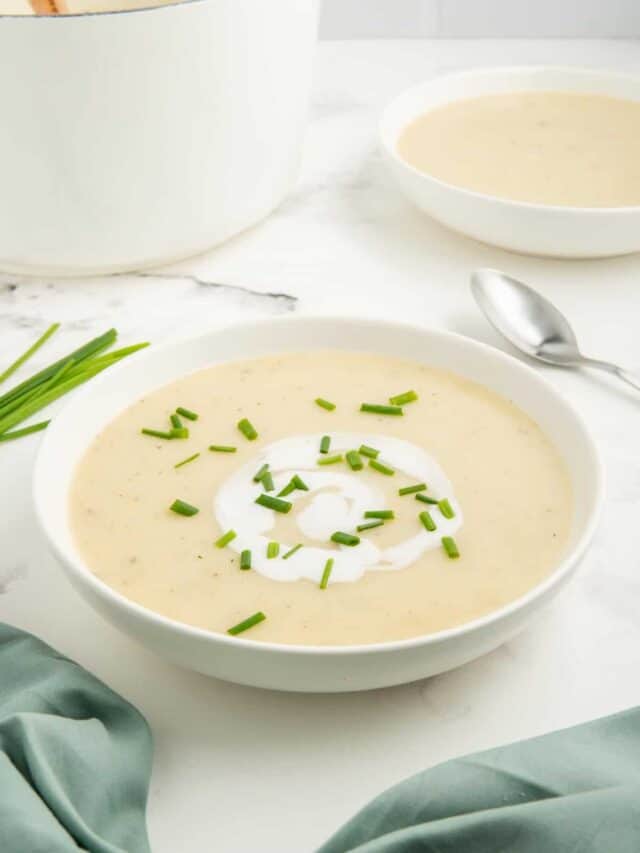 Potato and leek soup in a white bowl topped with coconut milk and chives.