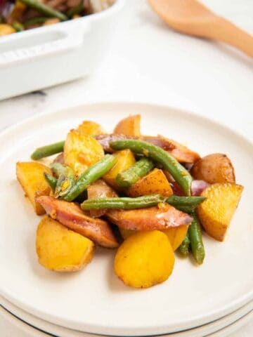 A close-up shot of sausage green bean potato casserole on a stack of white plates.