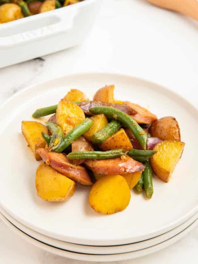 Sausage green bean and potato casserole on a stack of white plates.
