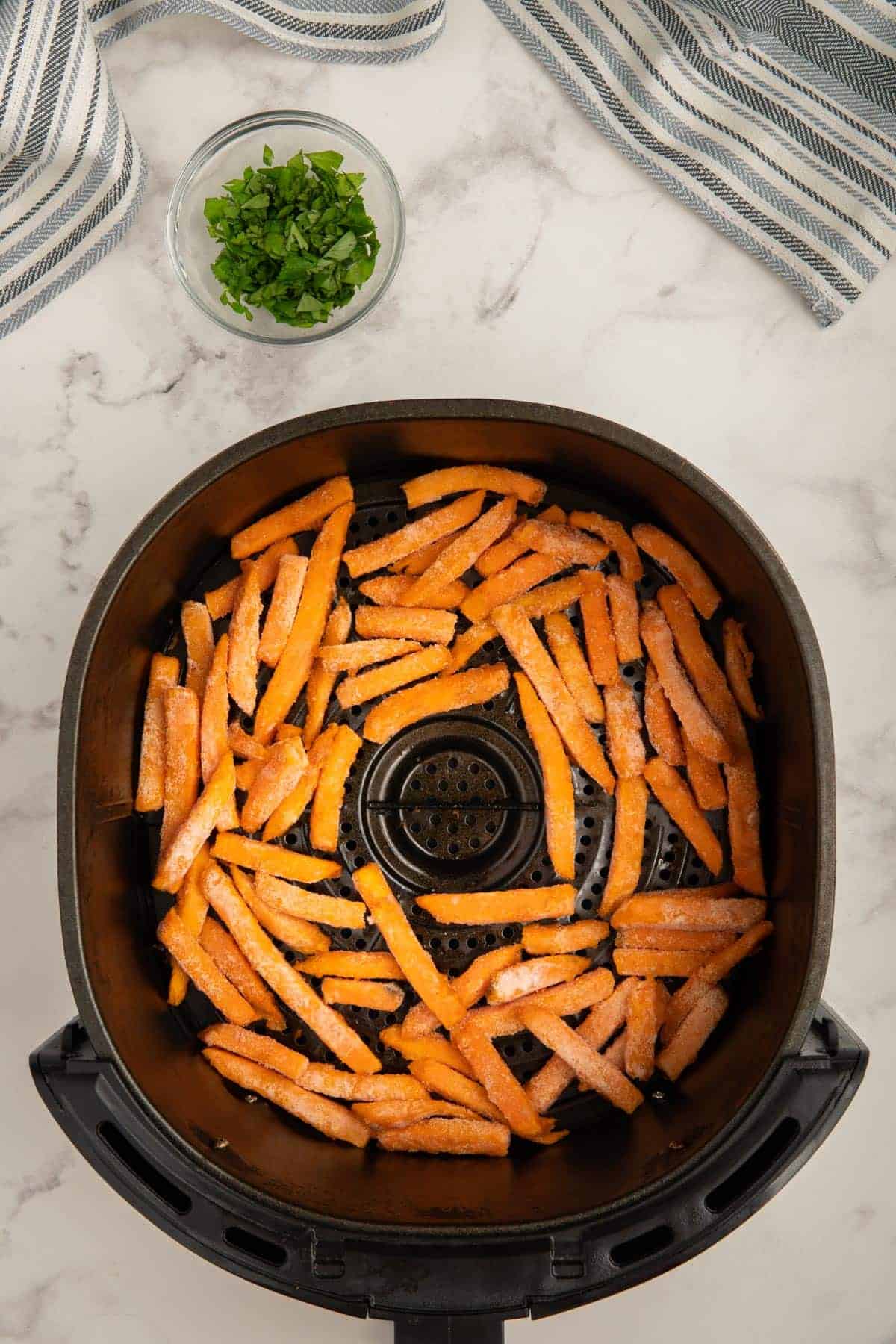 Frozen sweet potato fries in air fryer basket.