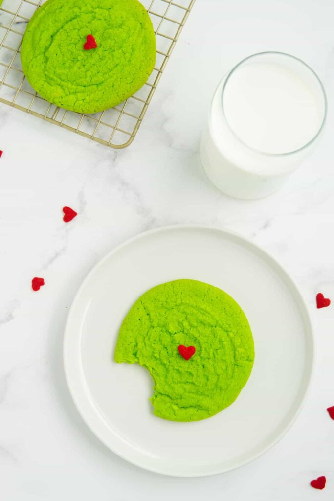 A single Grinch sugar cookie with a bit taken out on a white plate.
