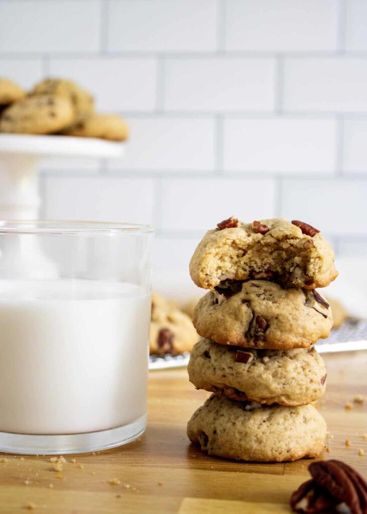 A stack of four maple pecan cookies with a glass of milk.