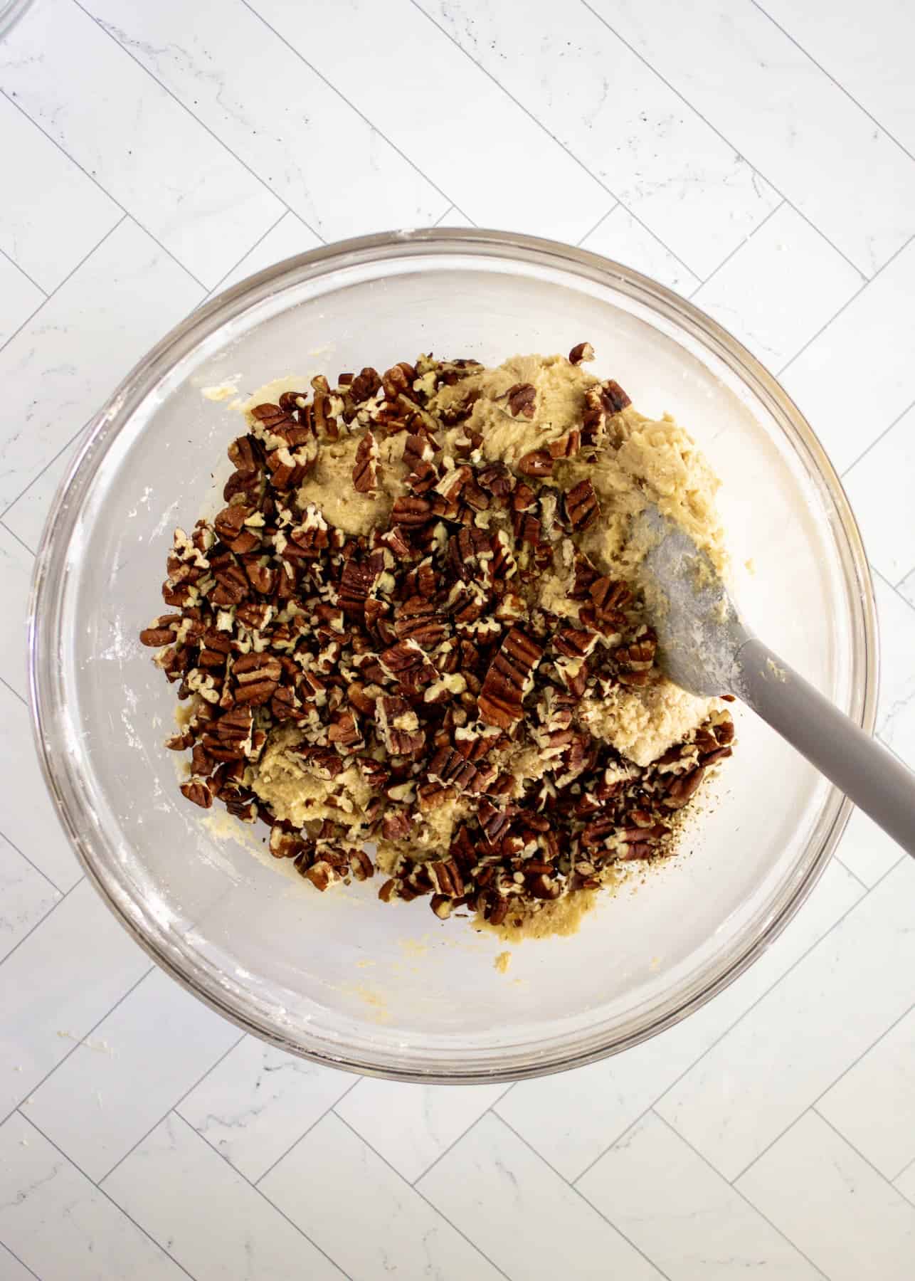 A glass bowl with cookie dough and chopped pecans unmixed.