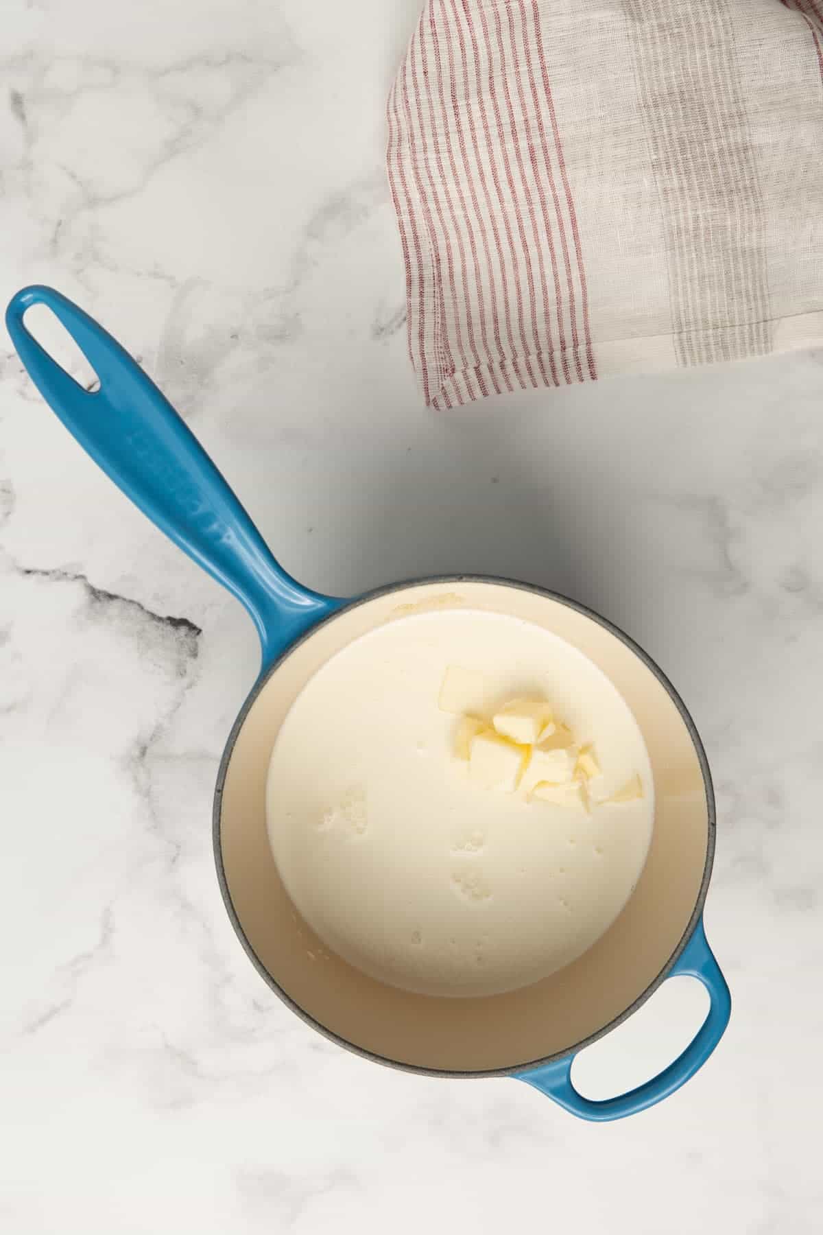 A blue Le Creuset saucepan containing heavy cream, butter, and chicken broth.