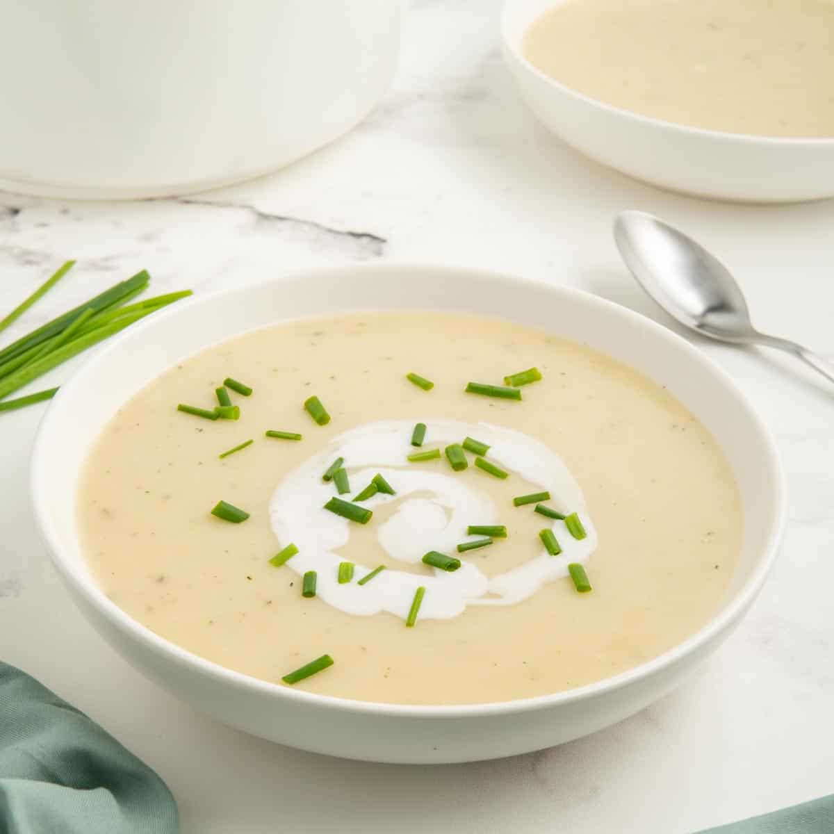 Potato and leek soup made with no cream in a white bowl with chives and a coconut milk swirl.