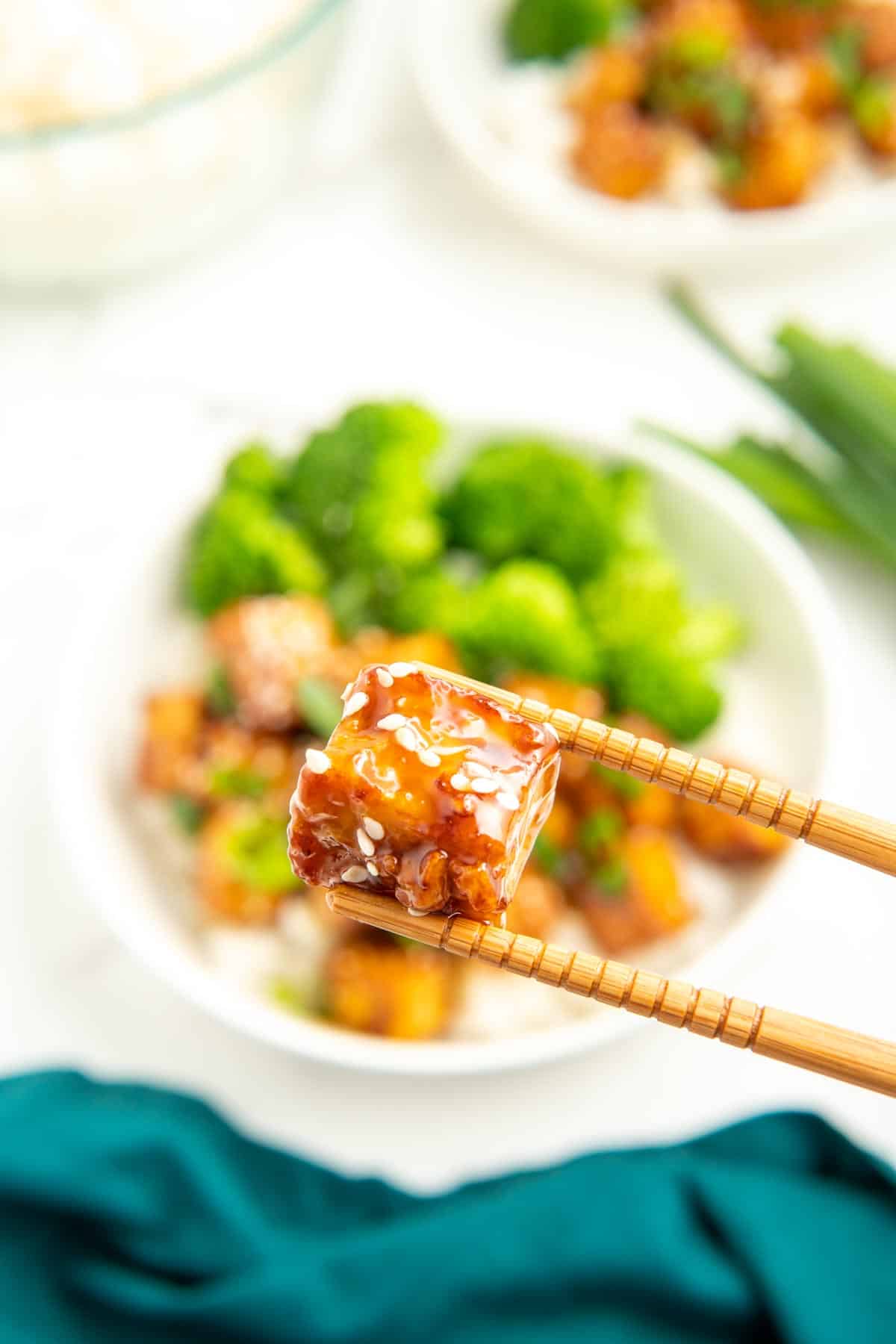 A close-up shots of a piece of sticky tofu being held up by chopsticks.