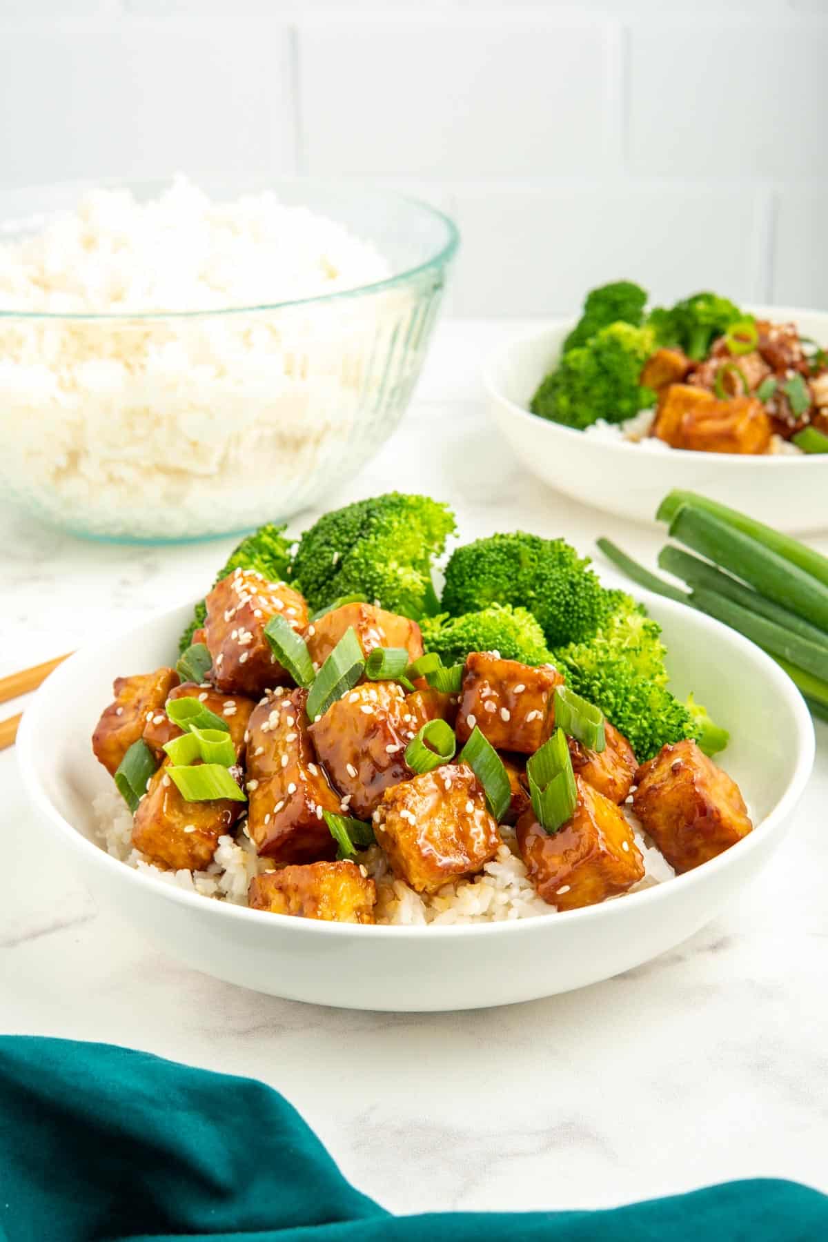 Sticky tofu served in a white bowl with rice and broccoli.
