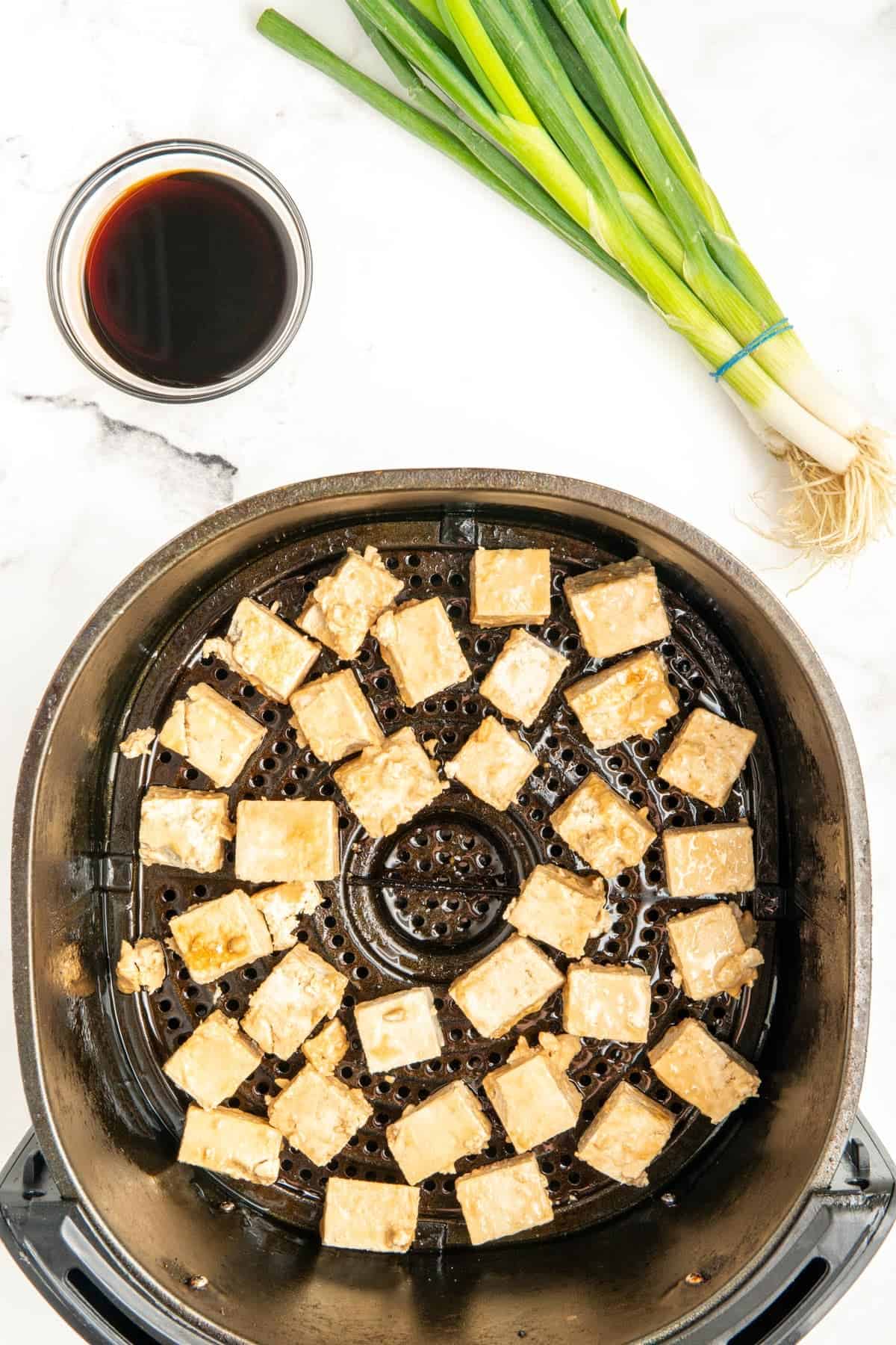 Uncooked tofu in an air fryer basket.