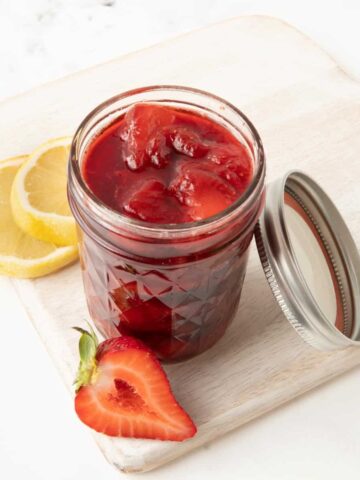 Strawberry compote in a glass jar with a fresh strawberry half and lemon slices.