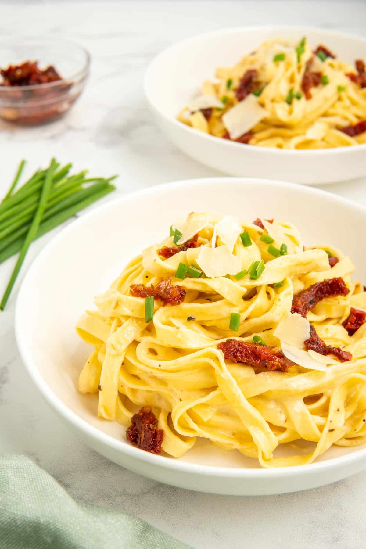 A bowl of sun-dried tomato alfredo pasta with chives and extra sun-dried tomatoes on top.