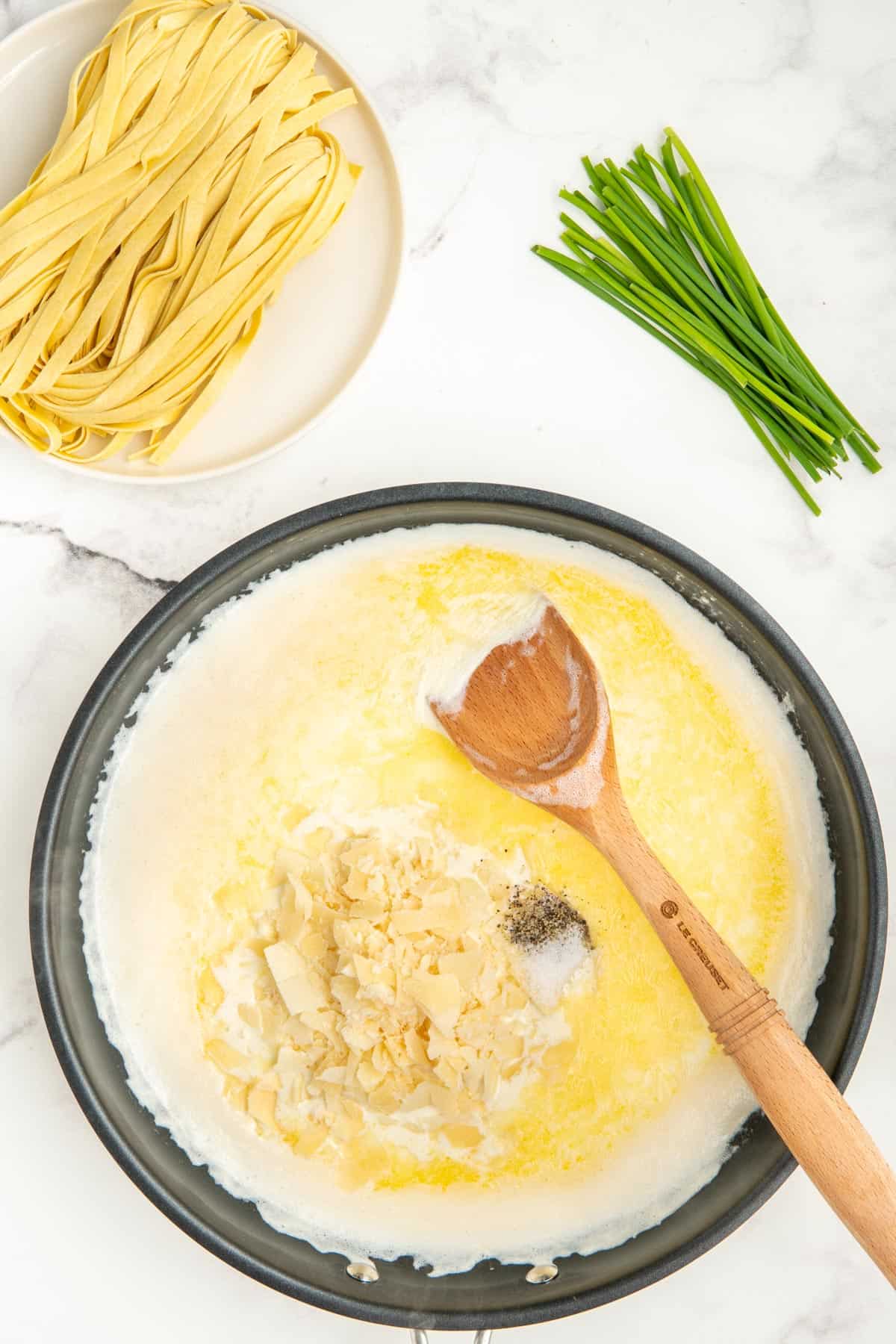 Parmesan cheese, salt, and pepper added to alfredo sauce in a non-stick frying pan.