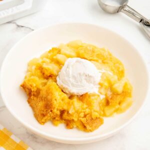 3 ingredient pineapple dump cake served in a white bowl with a scoop of coconut icecream.