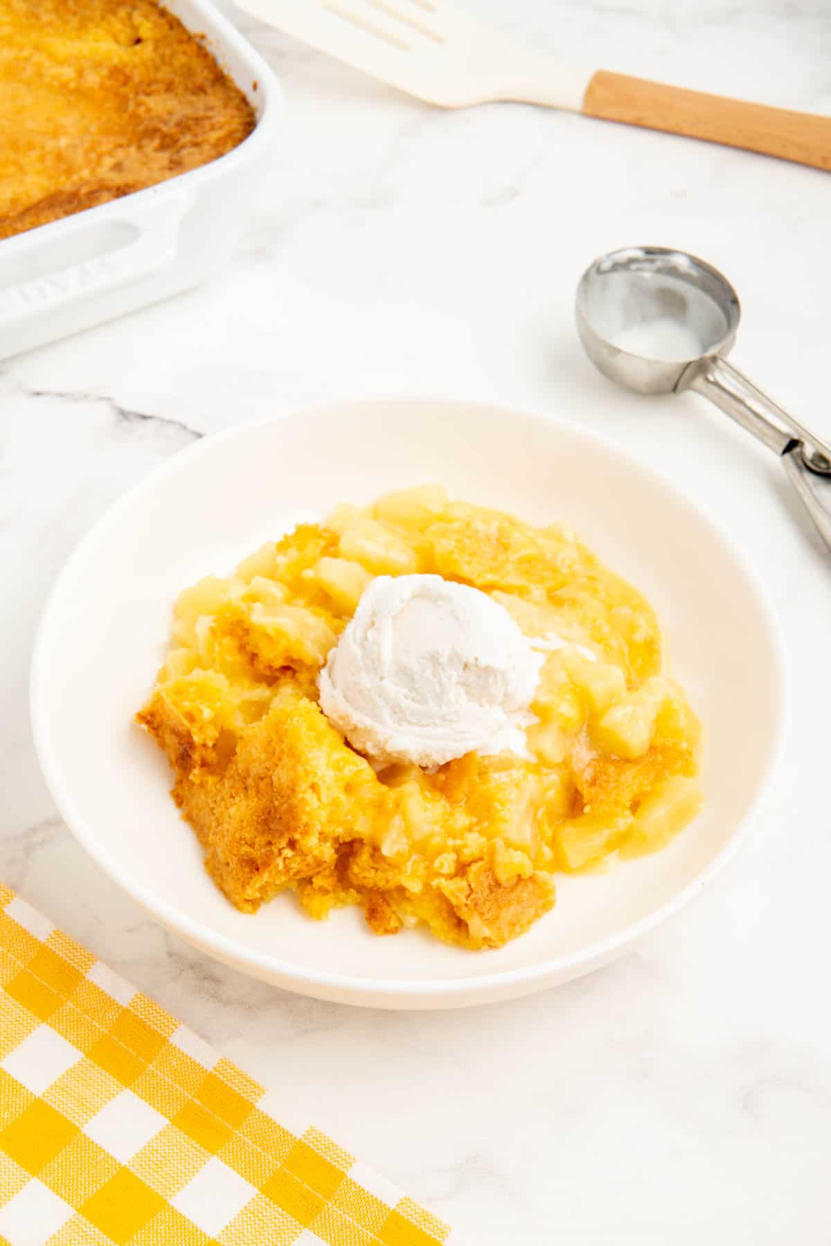 3 ingredient pineapple dump cake served with icecream in a white bowl.