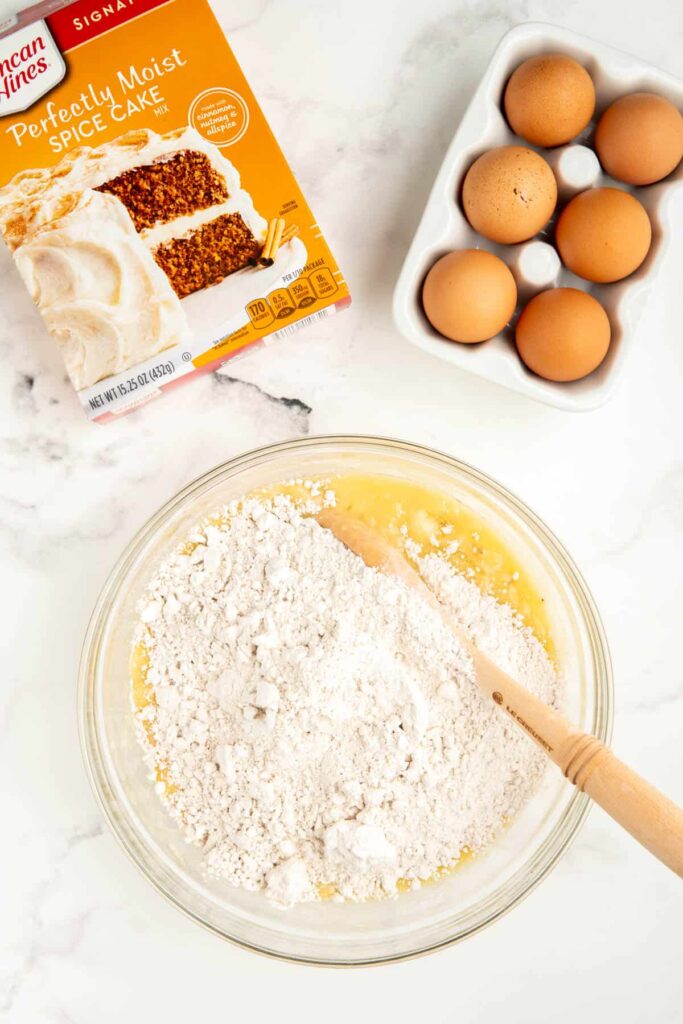Spice cake mix in a glass bowl with eggs, oil, and mashed bananas.