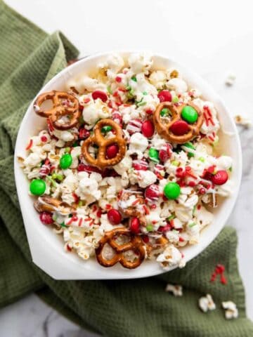 An overhead shot of Christmas popcorn mix in a white bowl.